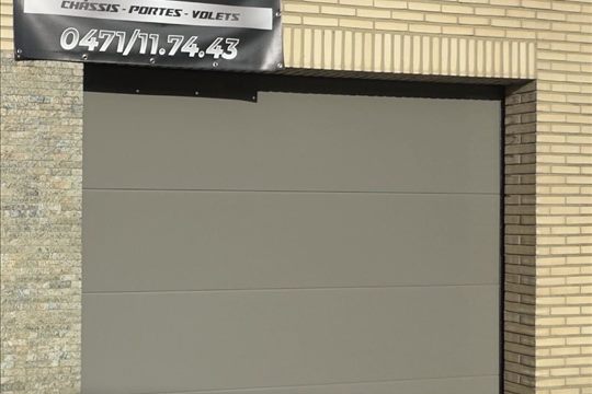 Porte de garage sectionnelle grise sur façade en briques claires — Braine-l'Alleud
