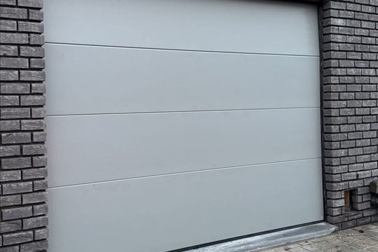 Porte de garage sectionnelle grise sur façade en briques noires — Quenast